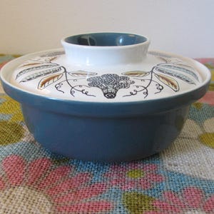 May include: A blue and white ceramic covered dish with a floral design. The dish has a white interior and a blue exterior with a floral pattern in brown and white.