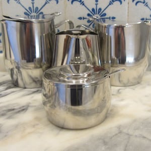 Conjunto de estilo moderno de meados do século XX composto por um bule de chá em aço inoxidável, uma chaleira/cafeteira, um açucareiro com tampa e uma leiteira - Fabricado na década de 1960.