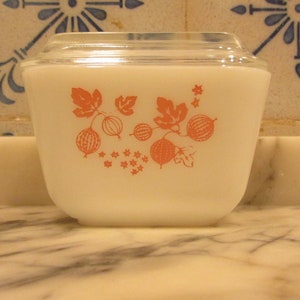 Może przedstawiać: Biała ceramiczna miska z pokrywką, ozdobiona wzorem różowych agrestów. Miska jest ozdobiona wzorem kwiatowym.