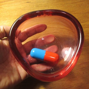 May include: A blue and red capsule pill in a clear glass bowl with a pink rim.
