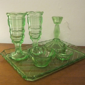 Könnte beinhalten: Ein grünes Glas-Schminkset mit zwei hohen Vasen, einer kleinen Schale, einer kleinen Schüssel und einem Kerzenhalter. Das Set befindet sich auf einem Holztablett.