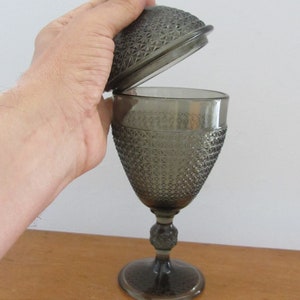 May include: A gray glass candy dish with a lid. The dish has a textured, diamond-shaped pattern. The lid is slightly ajar.