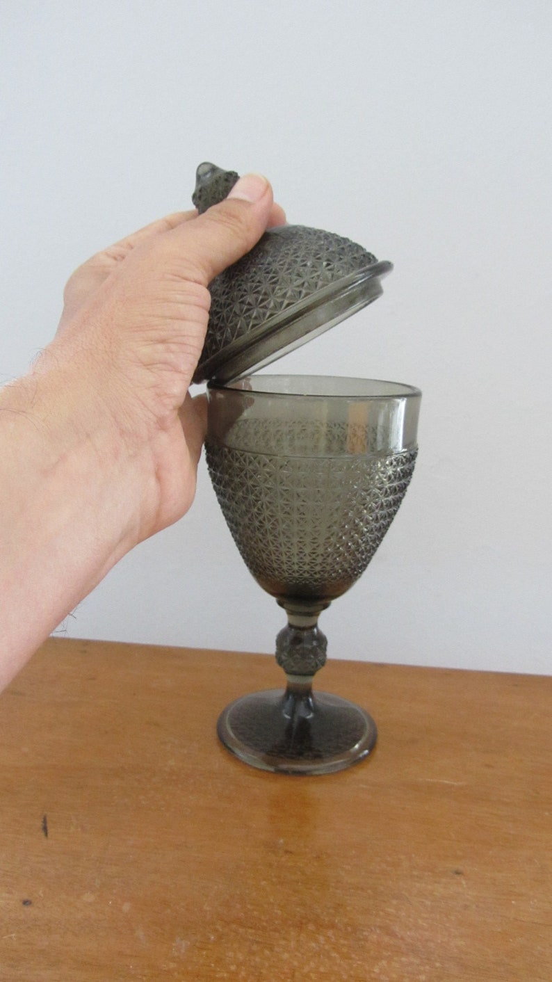 May include: A gray glass candy dish with a lid. The dish has a textured, diamond-shaped pattern. The lid is slightly ajar.