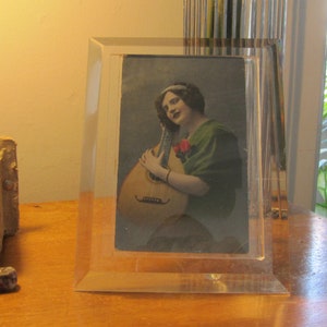 Könnte beinhalten: Ein gerahmtes Vintage-Foto einer Frau, die Gitarre spielt. Die Frau trägt ein grünes Kleid und hat dunkles Haar. Das Foto ist in einem klaren Acrylrahmen.