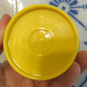 May include: Yellow plastic lid with a circular, raised, embossed design. The design features the words "Made in USA" and "&copy;1997" in a circle.
