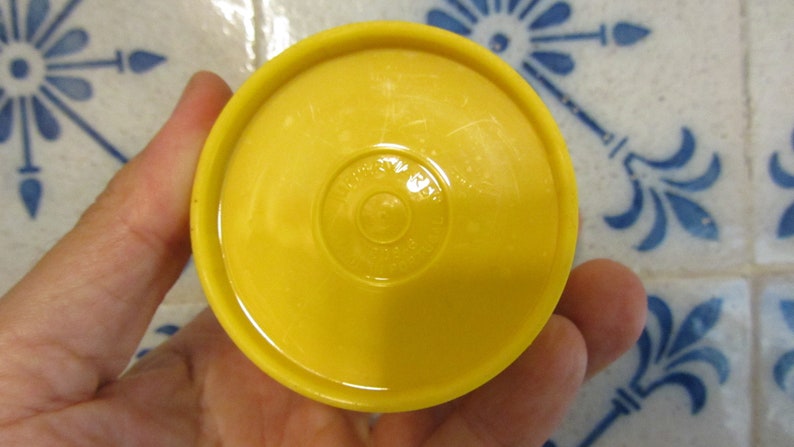 May include: Yellow plastic lid with a circular, raised, embossed design. The design features the words "Made in USA" and "&copy;1997" in a circle.