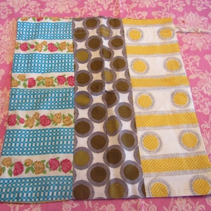 Könnte beinhalten: Eine Stofftasche mit drei verschiedenen gemusterten Paneelen. Das linke Paneel ist blau und weiß mit einem Blumendesign. Das mittlere Paneel ist braun und weiß mit einem Punkte-Design. Das rechte Paneel ist gelb und weiß mit einem Streifen-Design.