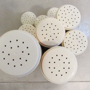 May include: A set of seven white plastic shaker lids with small holes. The lids are arranged in a circle on a light grey tiled surface.