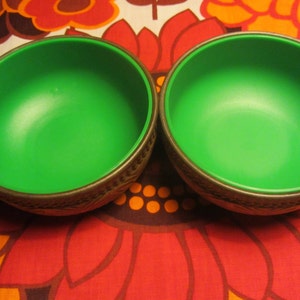 May include: Two green bowls with a brown rim and a decorative pattern. The bowls are on a red, orange, and white patterned background.