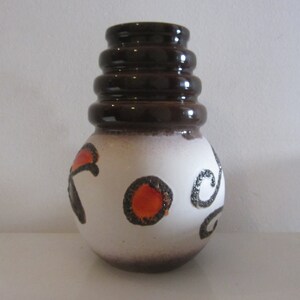 May include: A white ceramic vase with a brown rim and brown and orange abstract designs. The vase has a rounded body and a flared top.