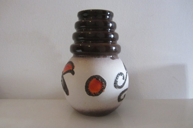 May include: A white ceramic vase with a brown rim and brown and orange abstract designs. The vase has a rounded body and a flared top.