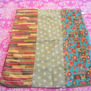 Könnte beinhalten: Eine Kordeltasche aus Stoff mit drei verschiedenen Mustern. Die linke Seite ist ein braunes, oranges und gelbes geometrisches Muster. Die Mitte ist ein grüner Stoff mit weißen Punkten. Die rechte Seite ist ein blauer Stoff mit orangefarbenen und gelben Blumen.