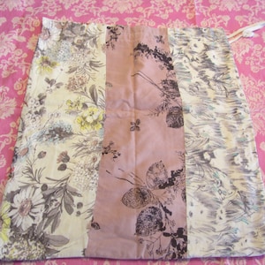 Könnte beinhalten: Ein Patchwork-Rock mit Blumen- und abstrakten Mustern in Creme, Grau und Mauve. Der Rock besteht aus zusammengenähten Stoffbahnen mit Kordelzug. Der Hintergrund ist ein rosa Blumenmuster.