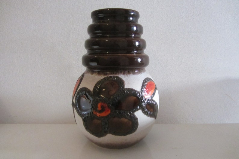 May include: A brown and white ceramic vase with a geometric pattern of flowers. The vase has a wide base and a narrow neck with a series of brown rings.