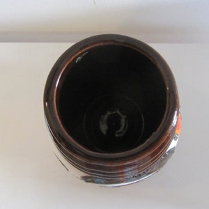 May include: A brown ceramic vase with a white and orange design. The vase has a wide opening and a rounded bottom.