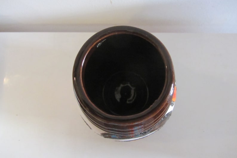 May include: A brown ceramic vase with a white and orange design. The vase has a wide opening and a rounded bottom.