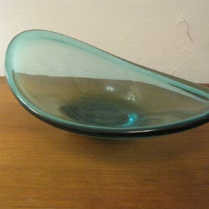 Pode incluir: Uma tigela de vidro azul turquesa com forma oval arredondada. A tigela é feita de vidro transparente com um leve tom verde.