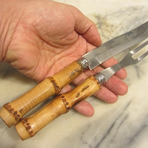 Könnte beinhalten: Ein Set aus zwei Küchenutensilien mit Bambusgriffen. Das Messer hat eine Klinge aus Edelstahl und die Gabel hat Zinken aus Edelstahl. Die Griffe sind hellbraun und haben eine strukturierte Oberfläche.