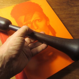 Könnte beinhalten: Ein dunkelbrauner Holzhammer mit einem abgerundeten Kopf und einem langen Stiel. Der Hammer wird von einer Hand gehalten.