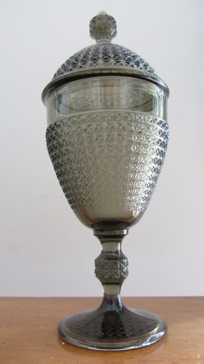May include: A gray glass candy dish with a lid. The dish has a diamond pattern and a pedestal base.
