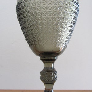 May include: A gray glass goblet with a diamond pattern. The goblet has a tall stem and a wide base.