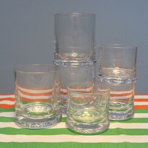 May include: A set of four clear glass tumblers with a textured rim. The tumblers are stacked on top of each other, with the largest tumbler at the bottom and the smallest tumbler at the top.