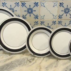 Könnte beinhalten: Satz von fünf weißen Keramik-Dinnertellern mit schwarzem Rand. Die Teller sind nach Größe geordnet, mit dem größten Teller hinten und dem kleinsten Teller vorne.