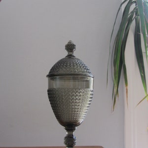 May include: A gray glass candy jar with a diamond pattern and a lid. The jar is on a wooden table.