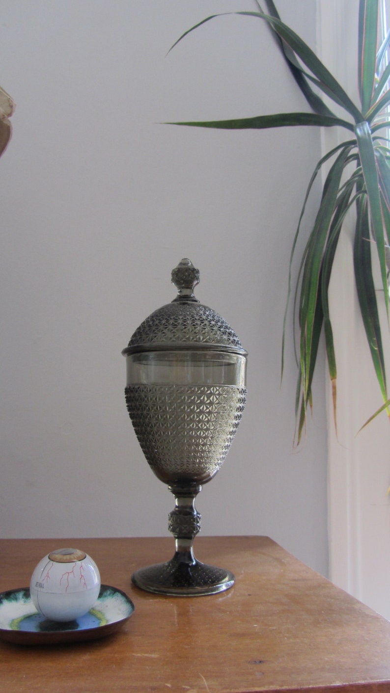May include: A gray glass candy jar with a diamond pattern and a lid. The jar is on a wooden table.