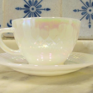 May include: A white iridescent teacup and saucer set with a delicate diamond pattern. The cup and saucer are made of opal glass and have a glossy finish.