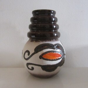 May include: A white ceramic vase with brown and orange geometric designs. The vase has a wide, round body and a tall, cylindrical neck with four stacked rings.