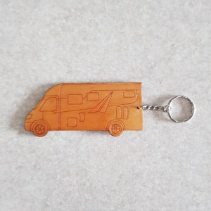 Puede incluir: Un llavero de cuero marr&oacute;n con forma de autocaravana. El llavero tiene un anillo de metal plateado.