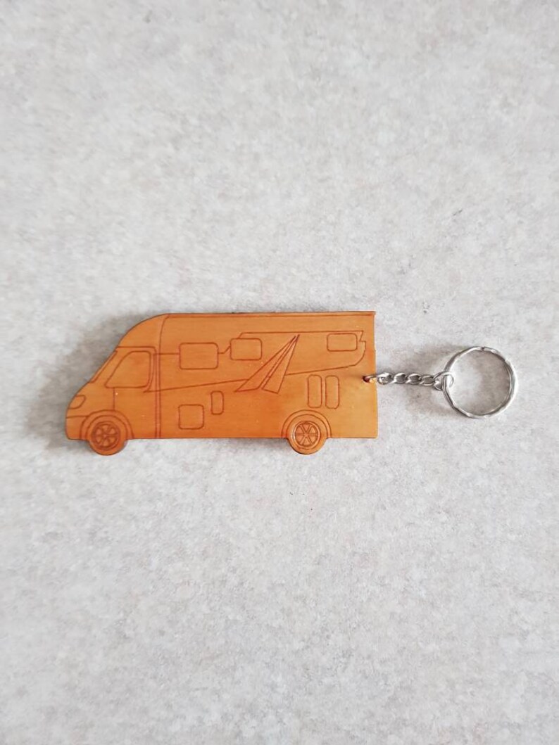 Puede incluir: Un llavero de cuero marr&oacute;n con forma de autocaravana. El llavero tiene un anillo de metal plateado.