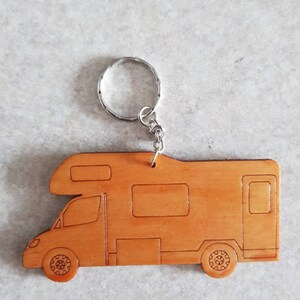 Puede incluir: Un llavero de madera con forma de autocaravana. El llavero es de color marr&oacute;n claro y tiene un llavero de plata.