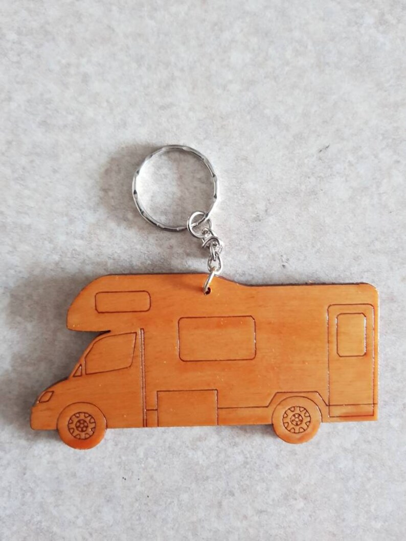 Puede incluir: Un llavero de madera con forma de autocaravana. El llavero es de color marr&oacute;n claro y tiene un llavero de plata.