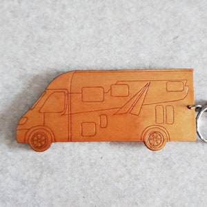 Puede incluir: Un llavero de cuero marr&oacute;n con forma de autocaravana. El llavero tiene un anillo de metal plateado.