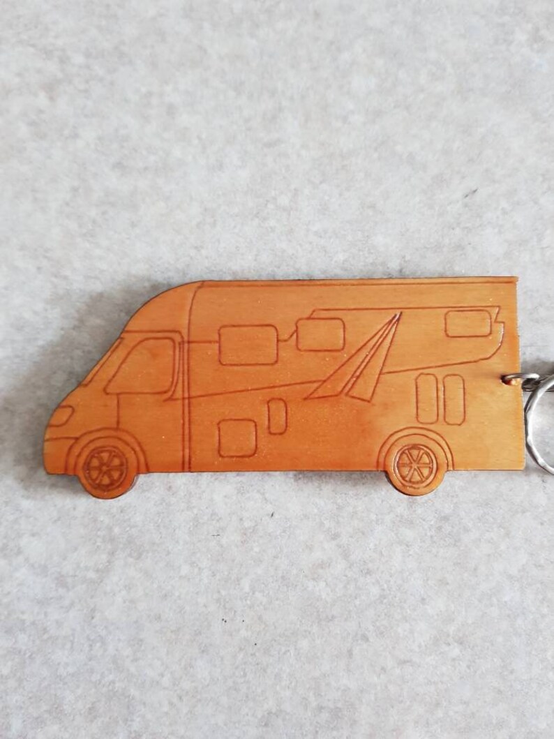 Puede incluir: Un llavero de cuero marr&oacute;n con forma de autocaravana. El llavero tiene un anillo de metal plateado.