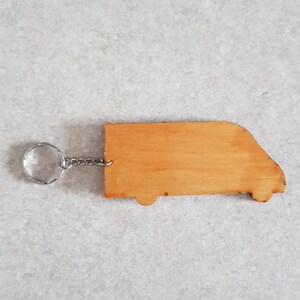Puede incluir: Un llavero de madera con forma de furgoneta con un anillo y una cadena de metal plateado.