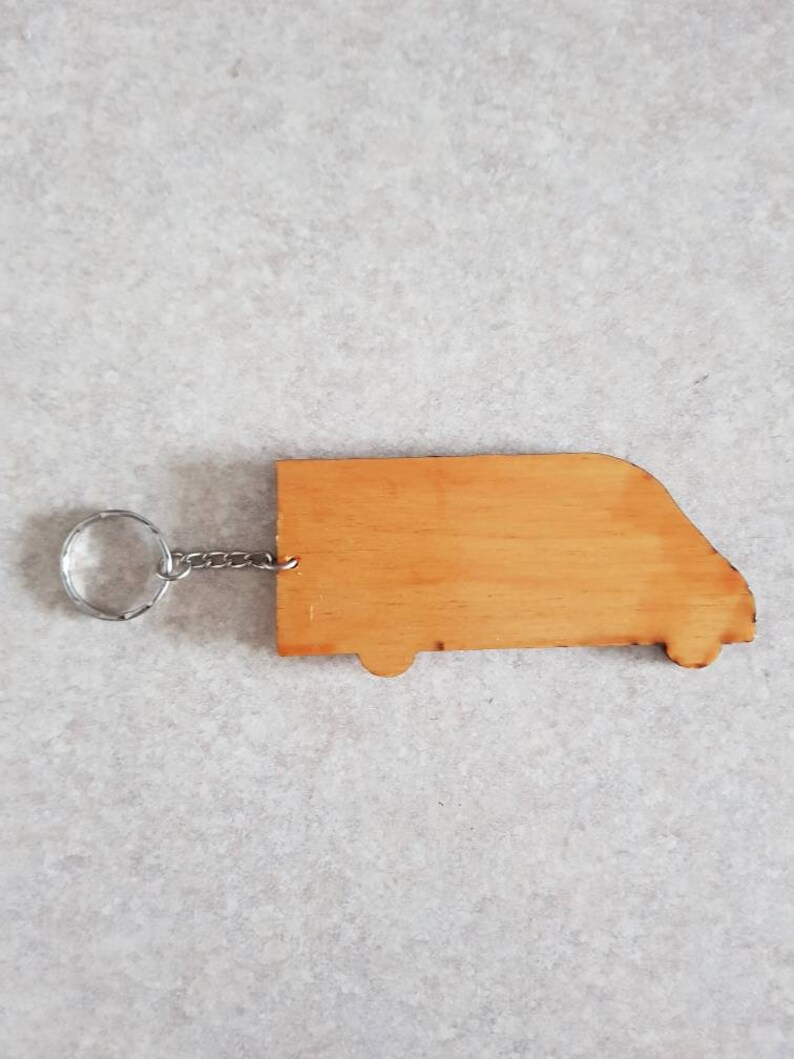 Puede incluir: Un llavero de madera con forma de furgoneta con un anillo y una cadena de metal plateado.