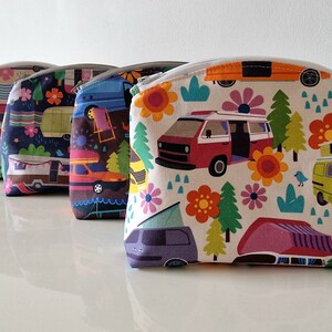 Könnte beinhalten: Vier farbenfrohe Reißverschlusstaschen mit einem Retro-Campingbus- und Blumenmuster. Die Taschen sind in einer Reihe auf einer weißen Oberfläche angeordnet.