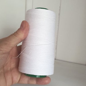 Pode incluir: Uma bobina de fio branco com uma bobina de plástico verde.