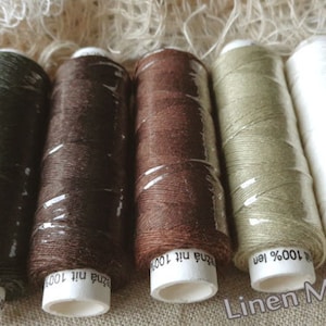 Può includere: Cinque bobine di filo di lino al 100% in varie tonalità di verde, marrone e bianco. Le bobine sono etichettate con il testo "100% len" e "žná nit 100%".
