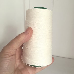 Può includere: Un'bobina di filo di cotone bianco con un top di plastica verde.