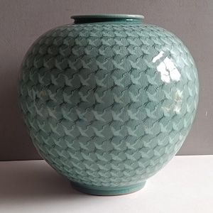 May include: A round, celadon green ceramic vase featuring a repeating pattern of flying cranes across its entire surface. The vessel has a smooth, glossy finish with a subtle crackle glaze effect and a wide, bulbous body with a narrow circular opening.