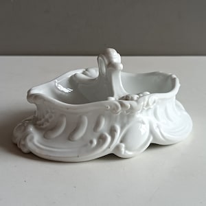 Può includere: Piatto in porcellana bianca con un manico decorativo e dettagli decorativi. Il piatto ha due scomparti ed è perfetto per servire condimenti o piccoli spuntini.