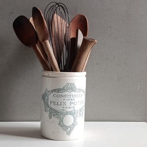 Könnte beinhalten: Ein weißer Keramik-Küchenutensilienhalter mit blauem Blumendesign und dem Text "CONFITURES FINES FELIX POTIN PARIS". Der Halter enthält Holzlöffel, einen Schneebesen und andere Küchenutensilien.