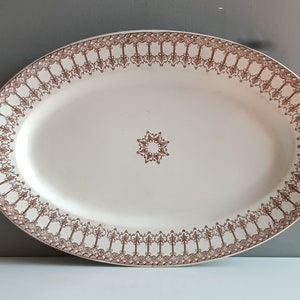 May include: A white oval serving platter with a brown decorative border and a brown starburst design in the center.