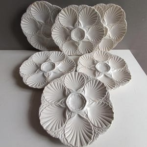 Puede incluir: Juego de seis platos de ostras de cerámica blanca con borde festoneado y un diseño en relieve de cinco conchas de ostras.