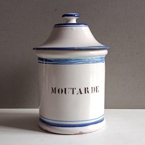 May include: A white ceramic jar with a lid, featuring blue stripes and the word "MOUTARDE" in black lettering. The jar has a cylindrical body and a conical lid, with a small knob on top. A classic kitchen storage container.