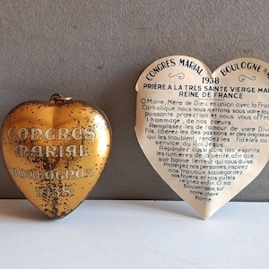 May include: A vintage heart-shaped gold-coloured religious pendant and a heart-shaped paper with French text. The pendant has the words "CONGRES MARIAL BOULOGNE 1938". The paper has a prayer to the Virgin Mary.